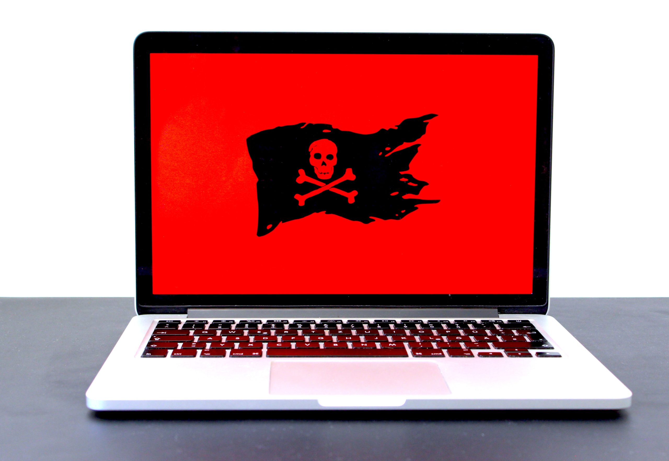 A laptop screen shows nothing but a black pirate flag against a bright red background.