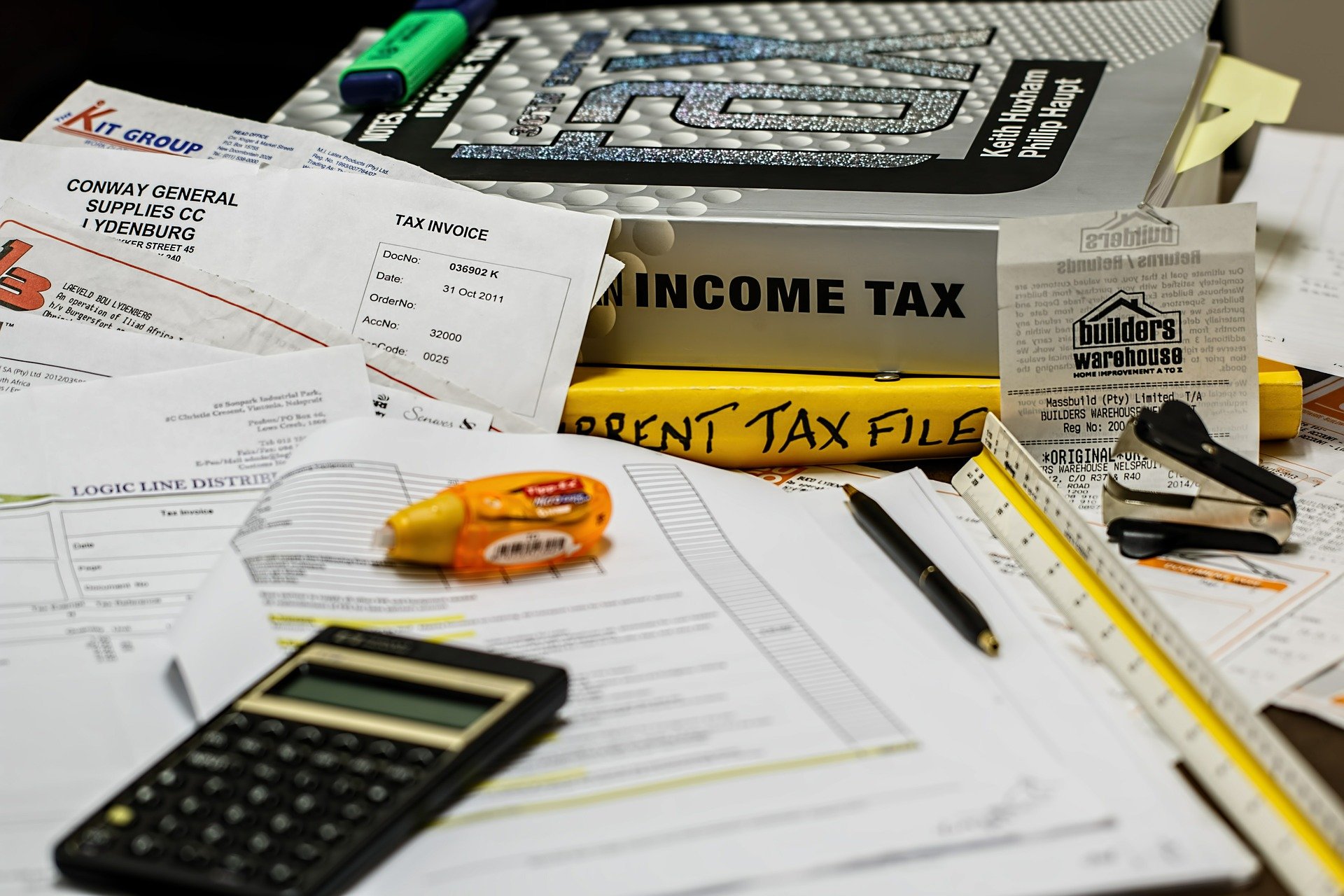 Tax books and invoices placed on a table with calculator and other stationery items lying alongside.