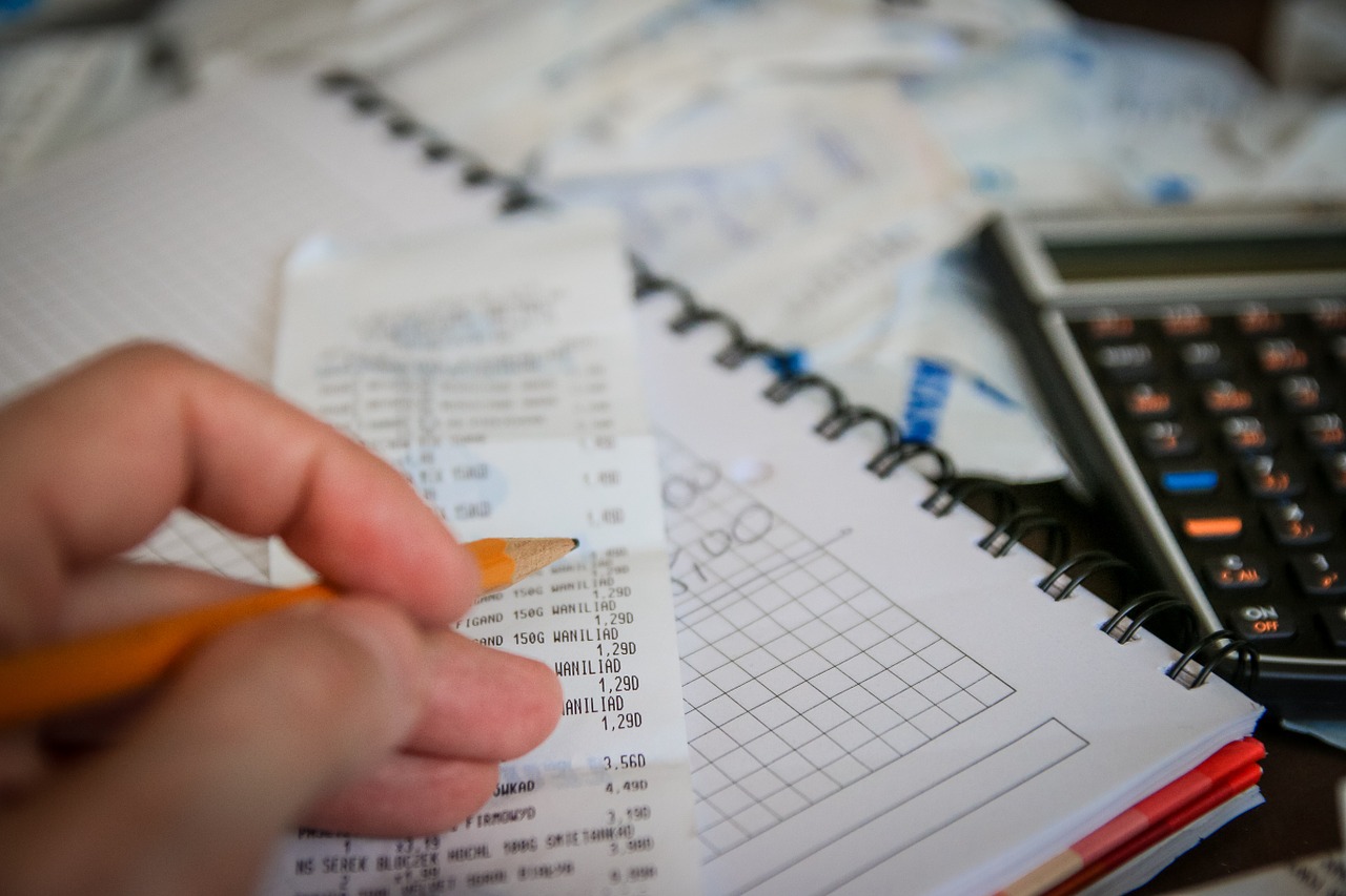Closeup of a person holding a pencil and calculating his business expenses.