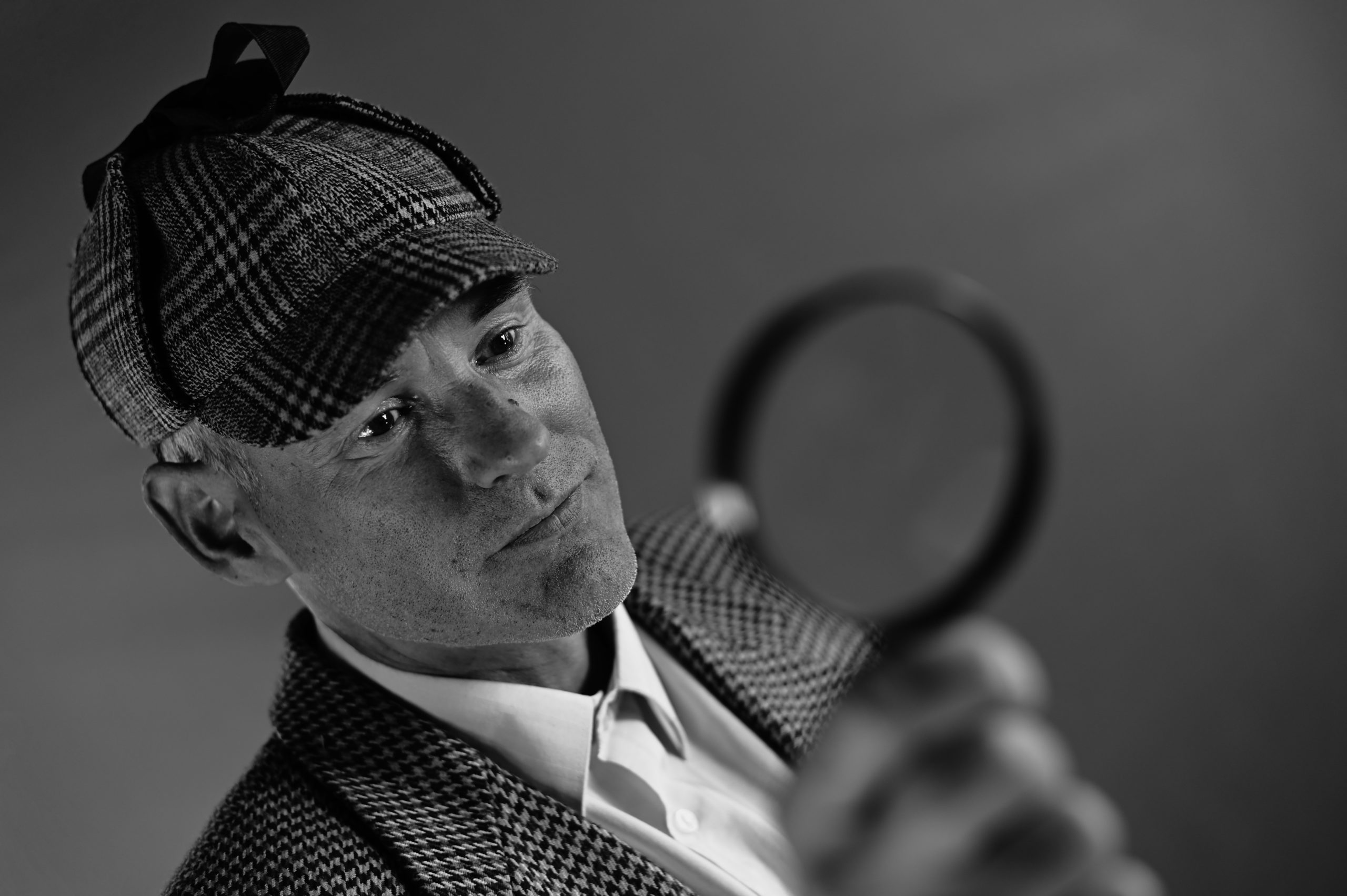 A man wearing a cap holds out a magnifying glass.