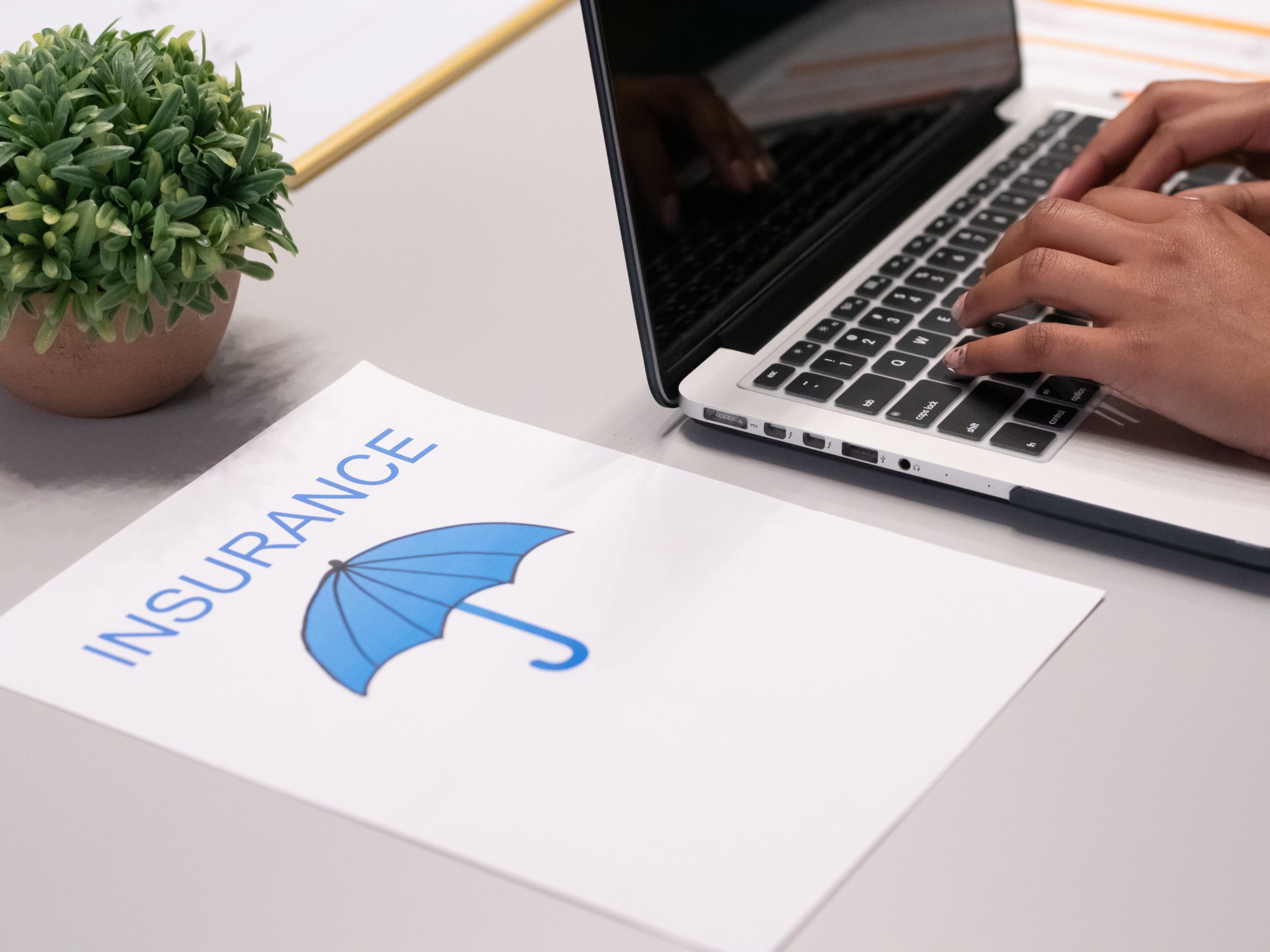Insurance written on a paper placed beside a person typing on a laptop