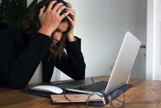 A seemingly stressed and frustrated woman, holding her head in front of a laptop