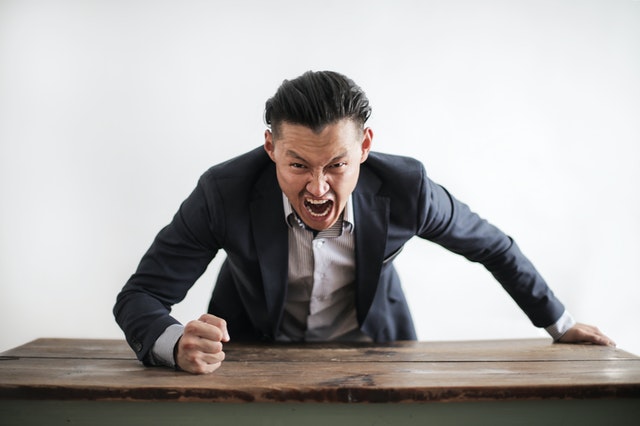 A man wearing a formal suit yelling and banging his fist on a table.