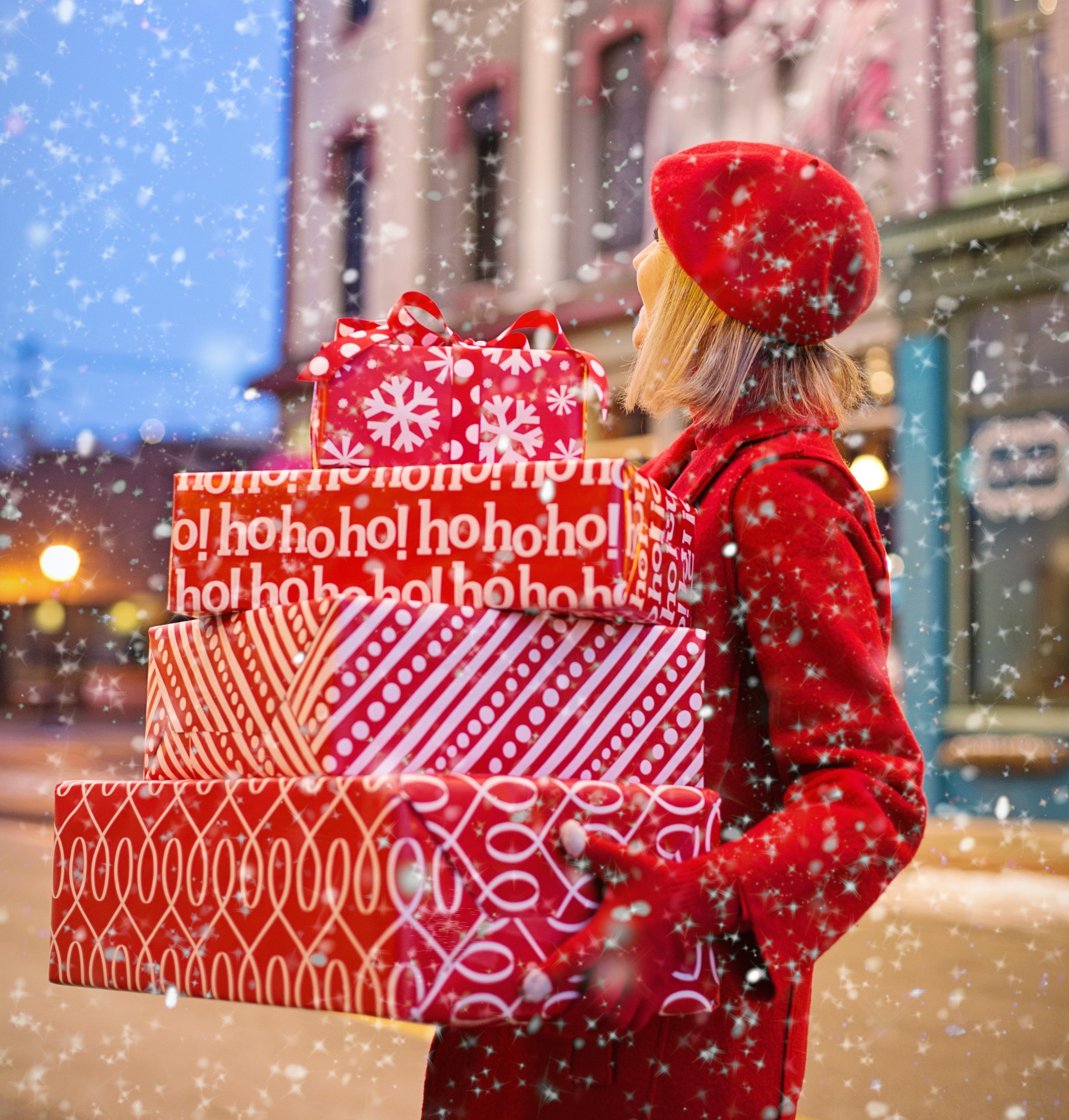 Woman stands in snow while holding three red Christmas-wrapped boxes.