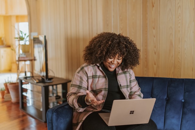 Woman sitting on couch with laptop on lap, smiling and having an online conversation
