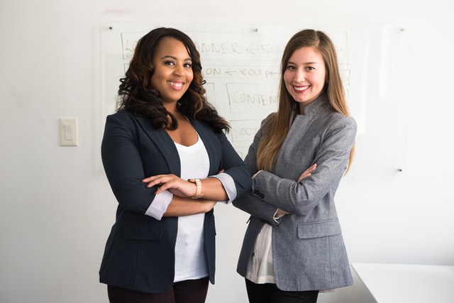 Two women in business suits standing beside a wall in the office.