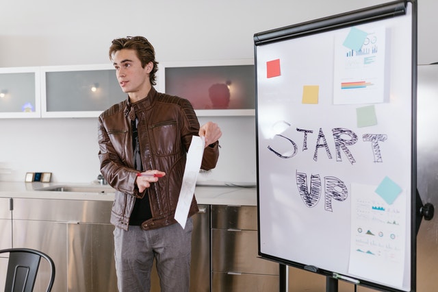 A young man gives a business pitch alongside a whiteboard that says “startup.”