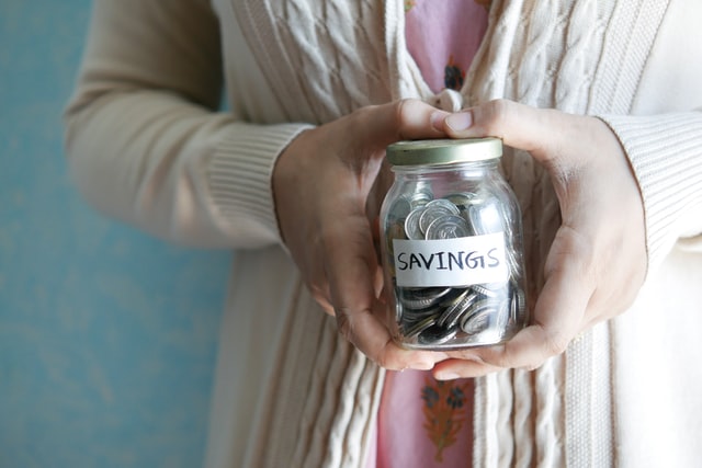 Woman holding a glass jar labeled “Savings” with coins in it.
