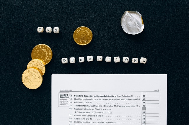 “Tax deductions” spelled with letter cubes placed on black textile surrounded by coins