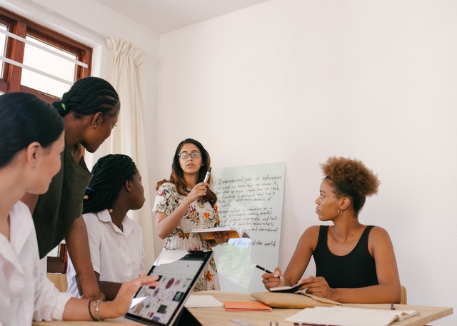 Woman presenting on white board while a bunch of others look on