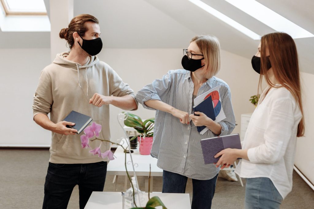 Co-workers wearing masks give one another elbow bumps in an office.