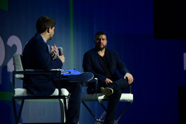 Two male professionals have a discussion on a stage.