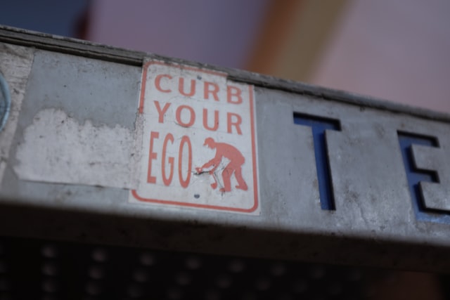 A red and white sign that says, “curb your ego.”