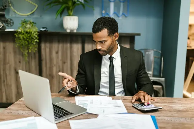A young man in a coat and tie sits working on a computer.