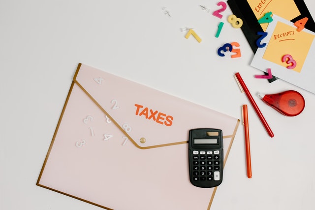 A black calculator placed on a folder with the words “taxes” written on it.