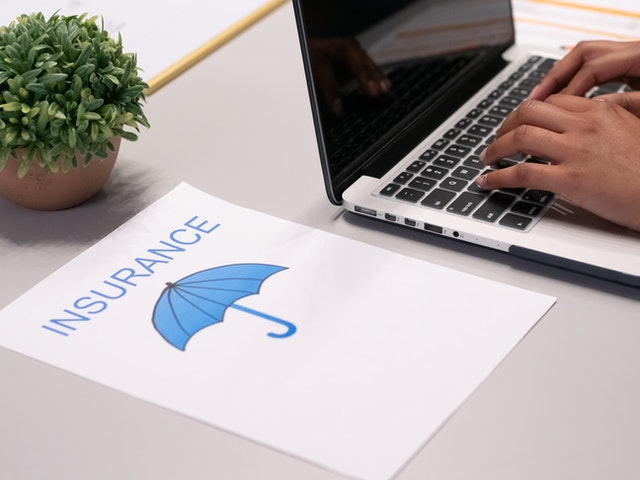 “Insurance” spelled on a paper lying beside a person typing on a laptop