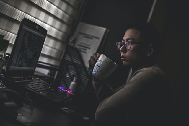 A man holding a cup of coffee looks with concern at his computer screen.