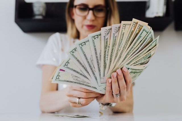 A female entrepreneur holding a wad of U.S. dollar bills in a fan shape.