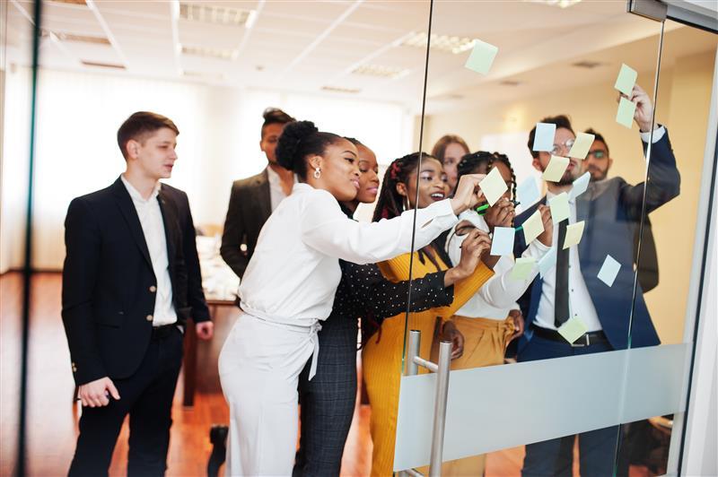 multicultural work team looking at post it notes on a glass wall in an office